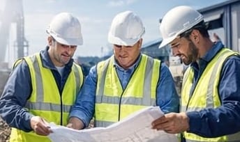 Personal de obra con casco y chaleco revisando planos en campo